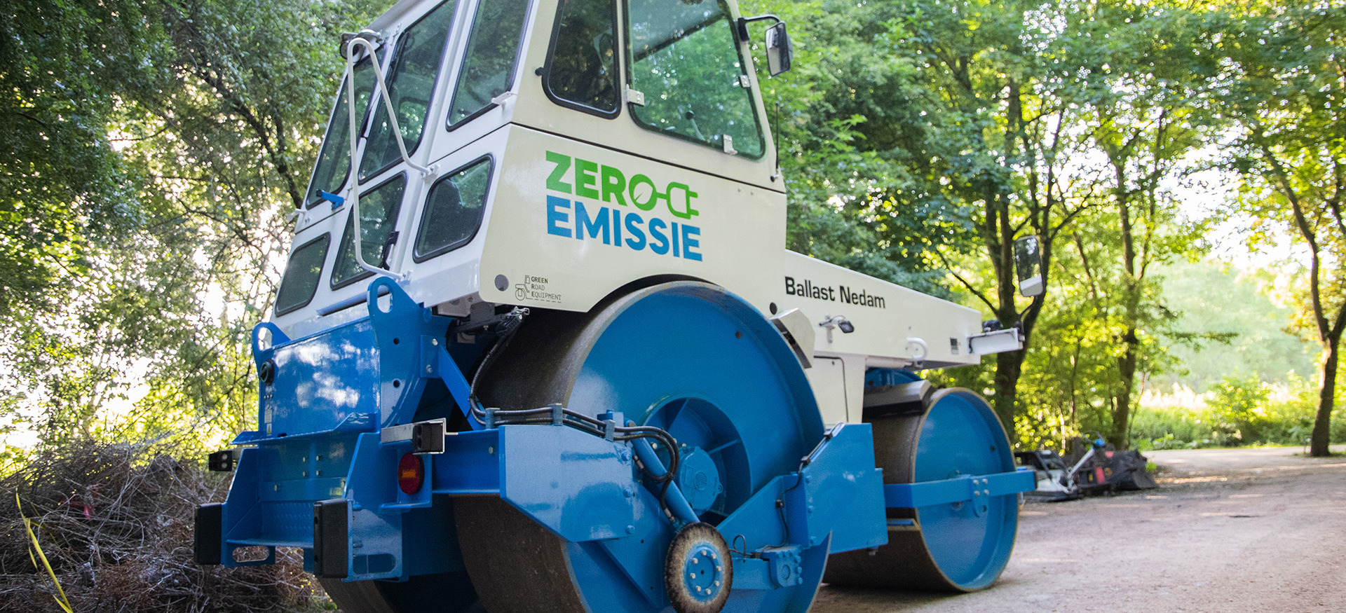 Bos met blauw witte asfaltwals met letters Zero Emissie op de zijkant